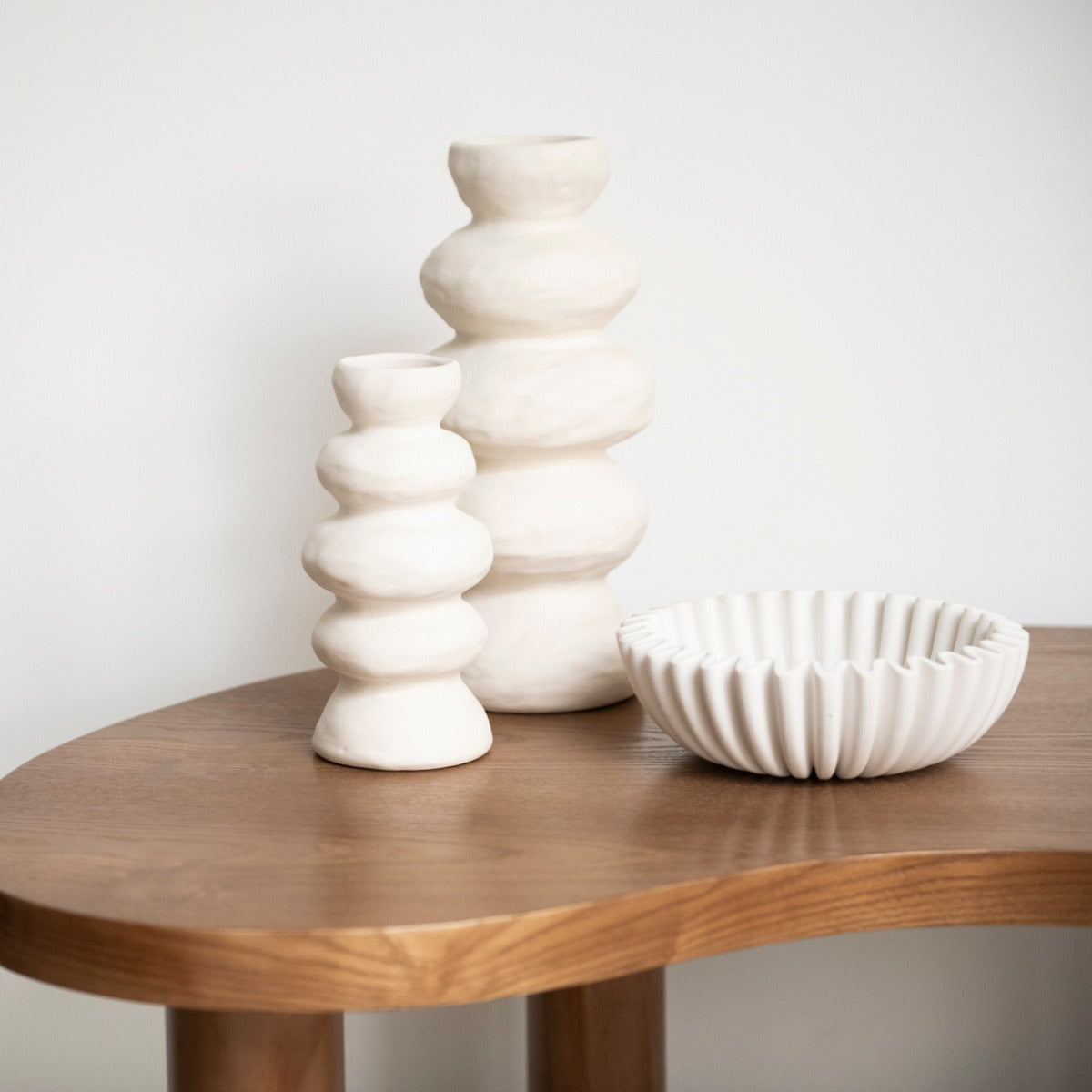 Jarrones decorativos blancos de formas redondeadas y cuenco de cerámica sobre mesa de madera