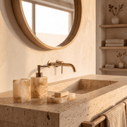 Set de baño efecto mármol en tonos crema sobre lavabo de piedra, con portacepillos, dispensador de jabón y jabonera