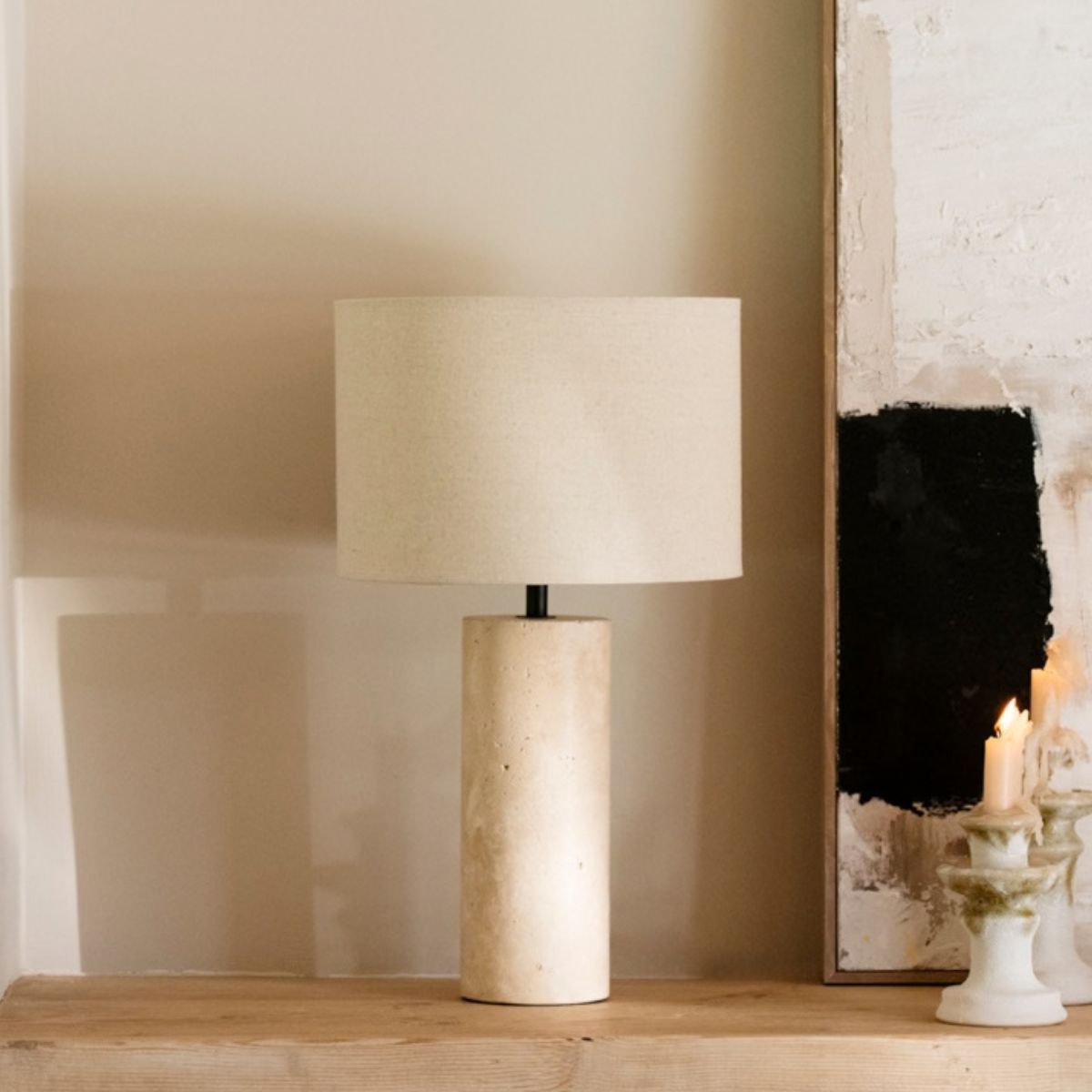 Lámpara de sobremesa de piedra beige con pantalla de tela, sobre mueble de madera en ambiente cálido.